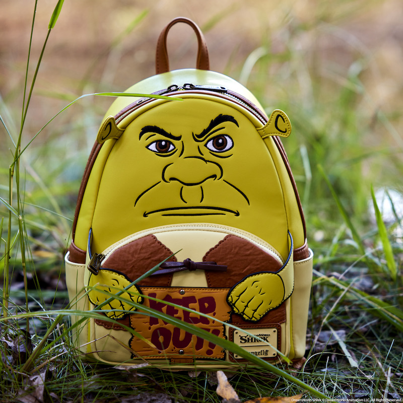 Image of the Loungefly Shrek Keep Out Cosplay ini Backpack sitting in a grassy, muddy area outside 